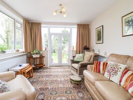 A cozy living room with a patterned carpet, leather sofas, a wooden side table, and a view through a glass door to a garden.