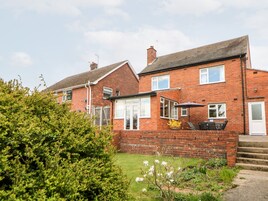 A two-story brick house with a front garden, a patio with outdoor furniture, and a visible chimney.