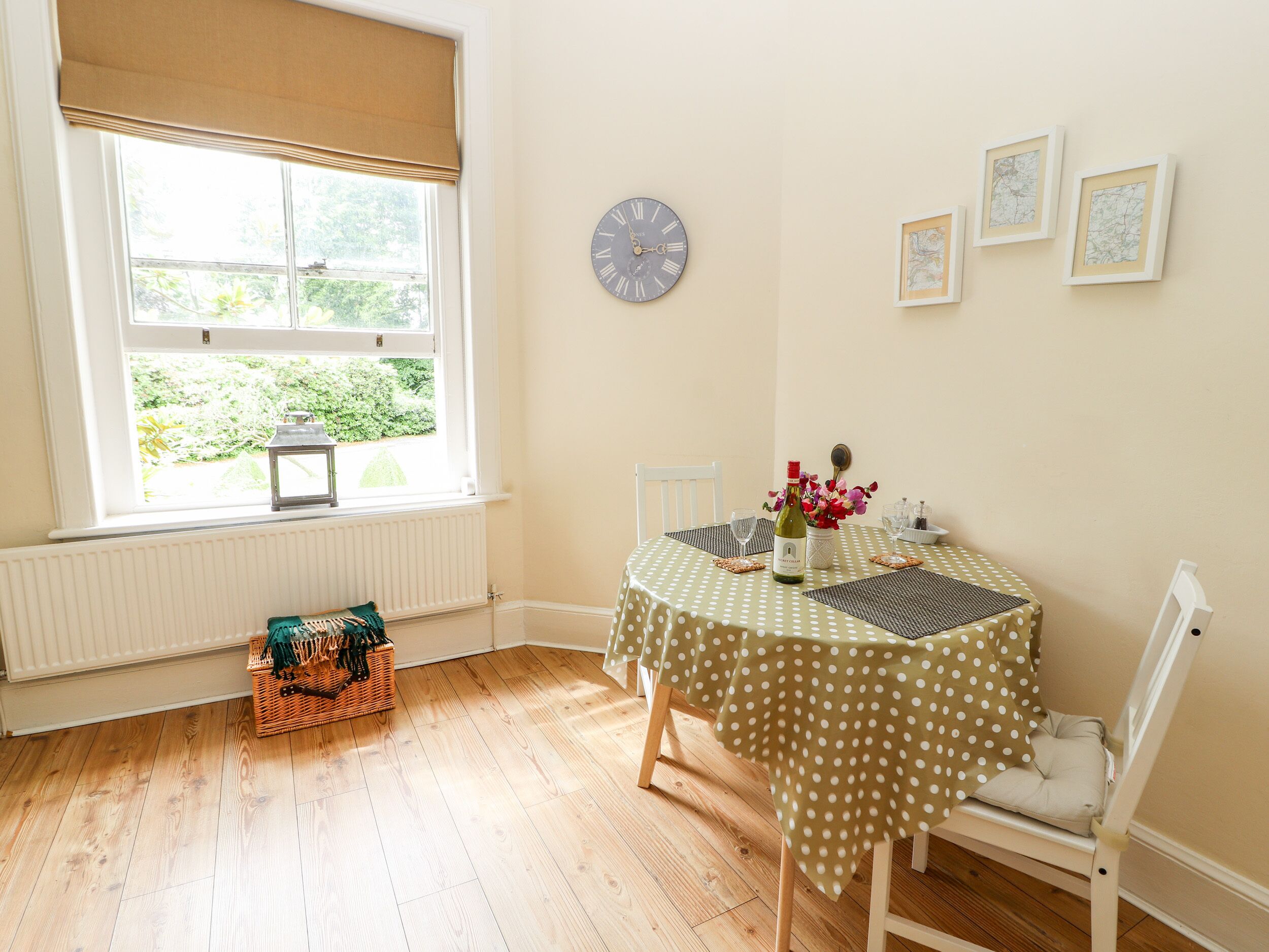 Comedor con una mesa lista para dos, un reloj en la pared y una ventana con vista a follaje.