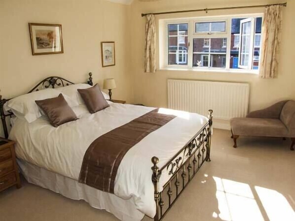 A bedroom with a bed, a nightstand, a lamp, a window with curtains, and a chair. - Harris House (Ludlow)