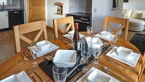 Comedor con mesa de madera dispuesta para cuatro personas, chimenea y cocina al fondo.