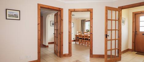 A spacious hallway with wooden doors, a tiled floor, and a dining area in the background.
