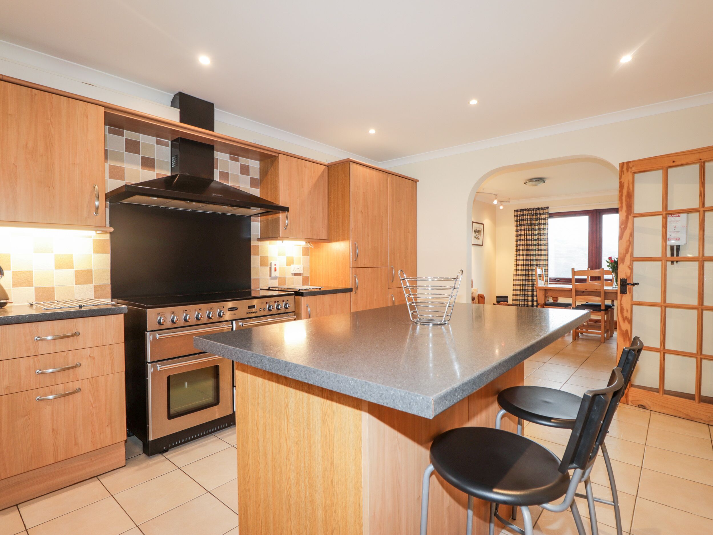 A modern kitchen with wooden cabinets, a large stove, and a central island with bar stools.