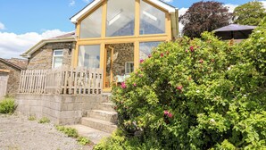 A stone house with a wooden fence, a glass door, and a garden with pink flowers. - Llety'r Wennol (Llanwrda)