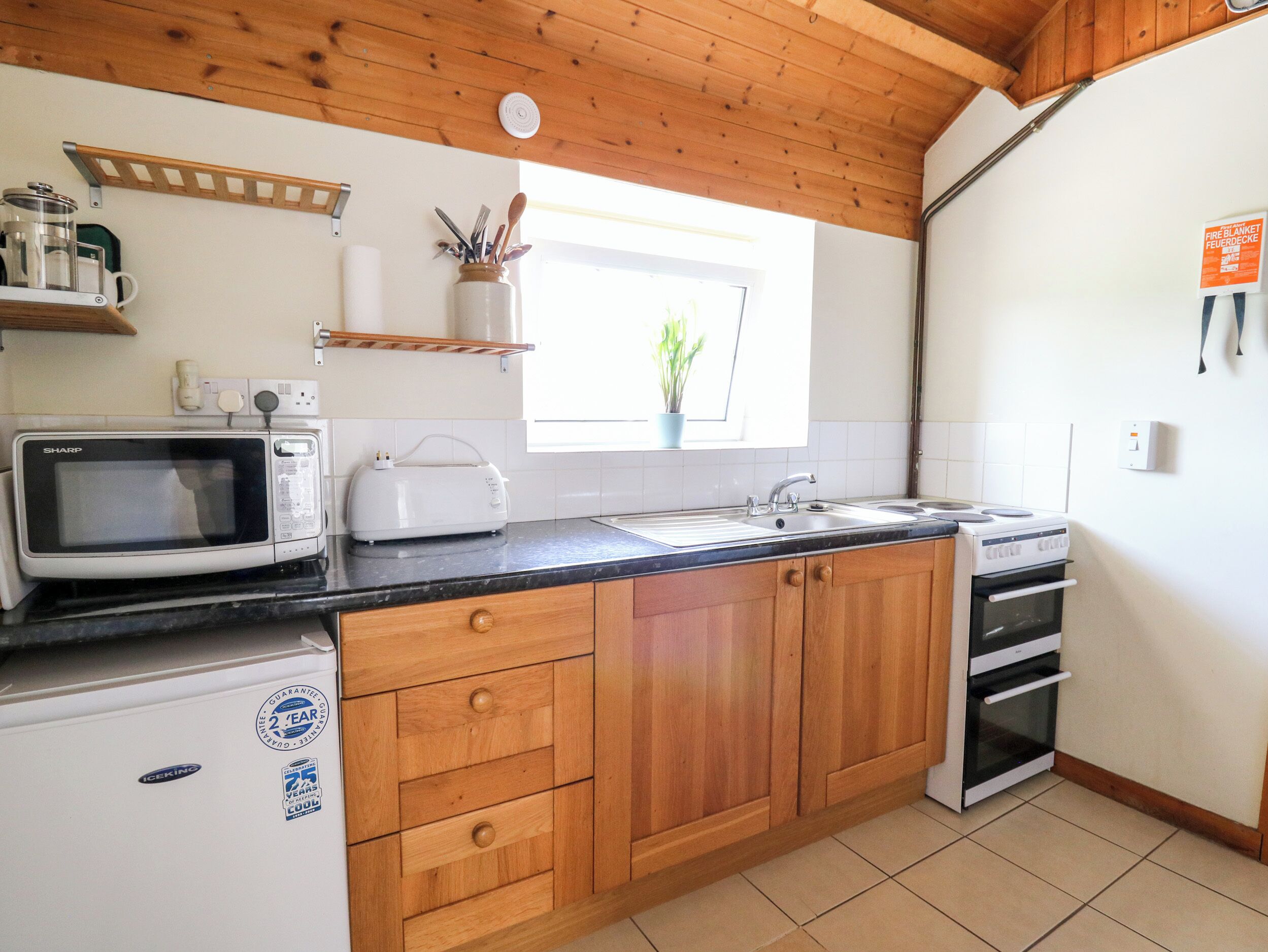 A compact kitchen with wooden cabinets, a microwave, toaster, sink, and a small refrigerator.