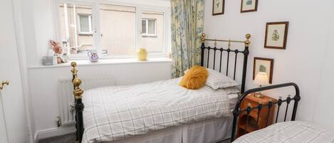 A bedroom with a bed, a window with curtains, a radiator, and framed pictures on the wall.