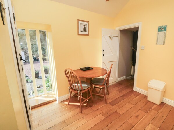 Quarto com piso de madeira, uma mesa redonda com cadeiras, uma porta e uma janela com vista para o verde lá fora.