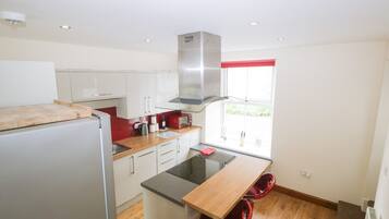 Una cocina compacta con armarios blancos, una campana extractora de acero inoxidable, una encimera de madera y una ventana con cortina roja.