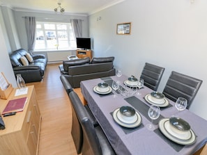 A dining area with a table set for four, a sofa, and a television in the background.