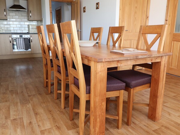 Une table à manger en bois, avec six chaises, un coin cuisine équipé d’une cuisinière et de placards, et un plancher en bois.