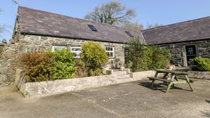 A stone building with a sloped roof, a small window, and a picnic table in the foreground. - Bwthyn yr Helyg (Pwllheli)