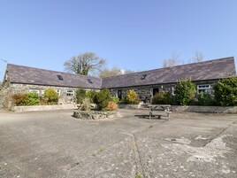 A stone building with a paved courtyard, two picnic tables, and a small garden area.