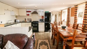 A compact kitchen with modern appliances, a dining area with wooden furniture, and a cozy living space with a leather couch. - Bwthyn yr Helyg (Pwllheli)