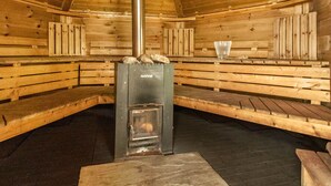 A wooden sauna with benches, a central heating unit labeled 'HARVIA', and a glass on the bench. - Eden Lodge (Ulverston)