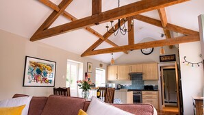 A spacious living area with a high ceiling and exposed wooden beams, a cozy sofa with yellow cushions, and a kitchen in the background. - Alwent Mill (Darlington)