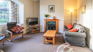 A living room with a fireplace, a television, a sofa, a chair, and a table. - Pensychnant Cottage (Conwy)
