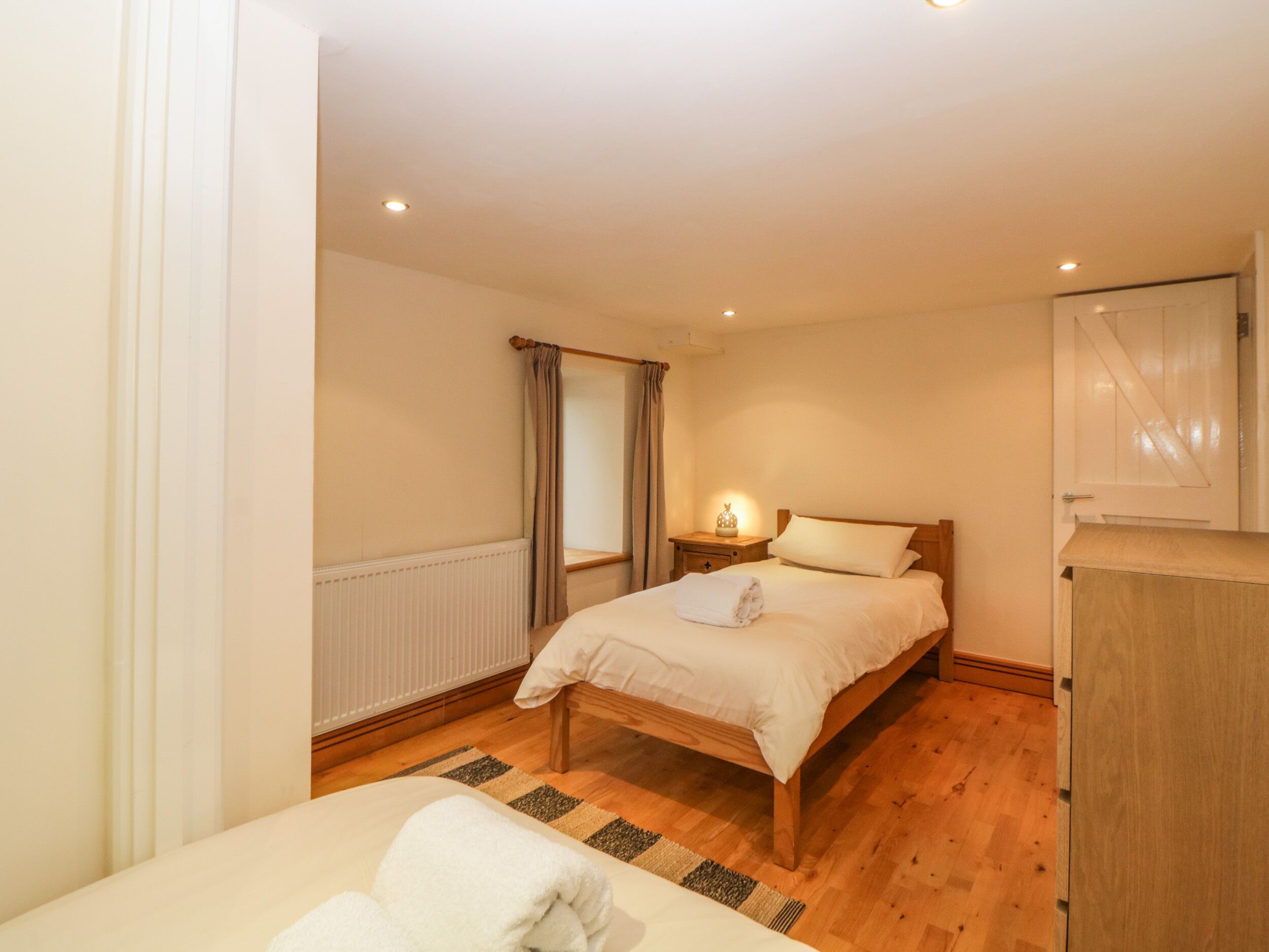 A bedroom with a wooden bed, a nightstand with a lamp, a radiator, and a wardrobe.