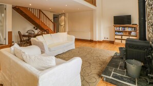 A spacious living room with a white sofa, a fireplace, a bookshelf, and a staircase leading to an upper level. - Meader Barn (Tavistock)