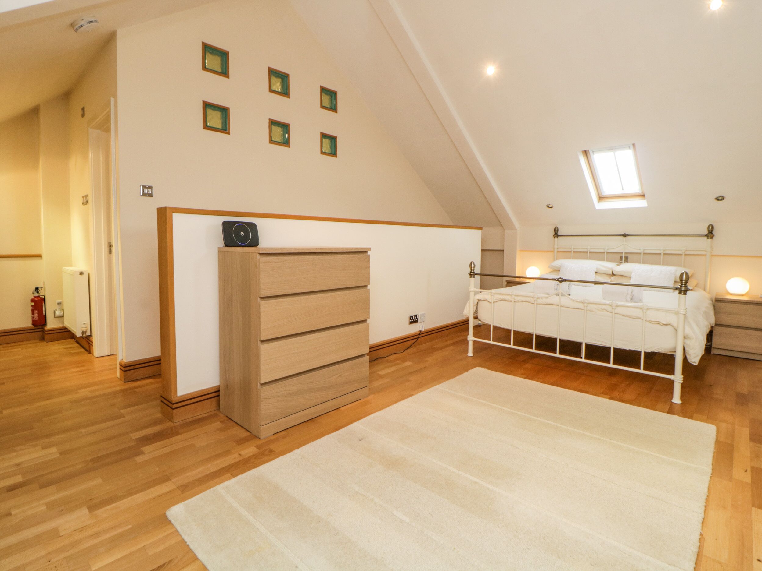 A bedroom with a wooden dresser, a white bed, a skylight, and a small window.