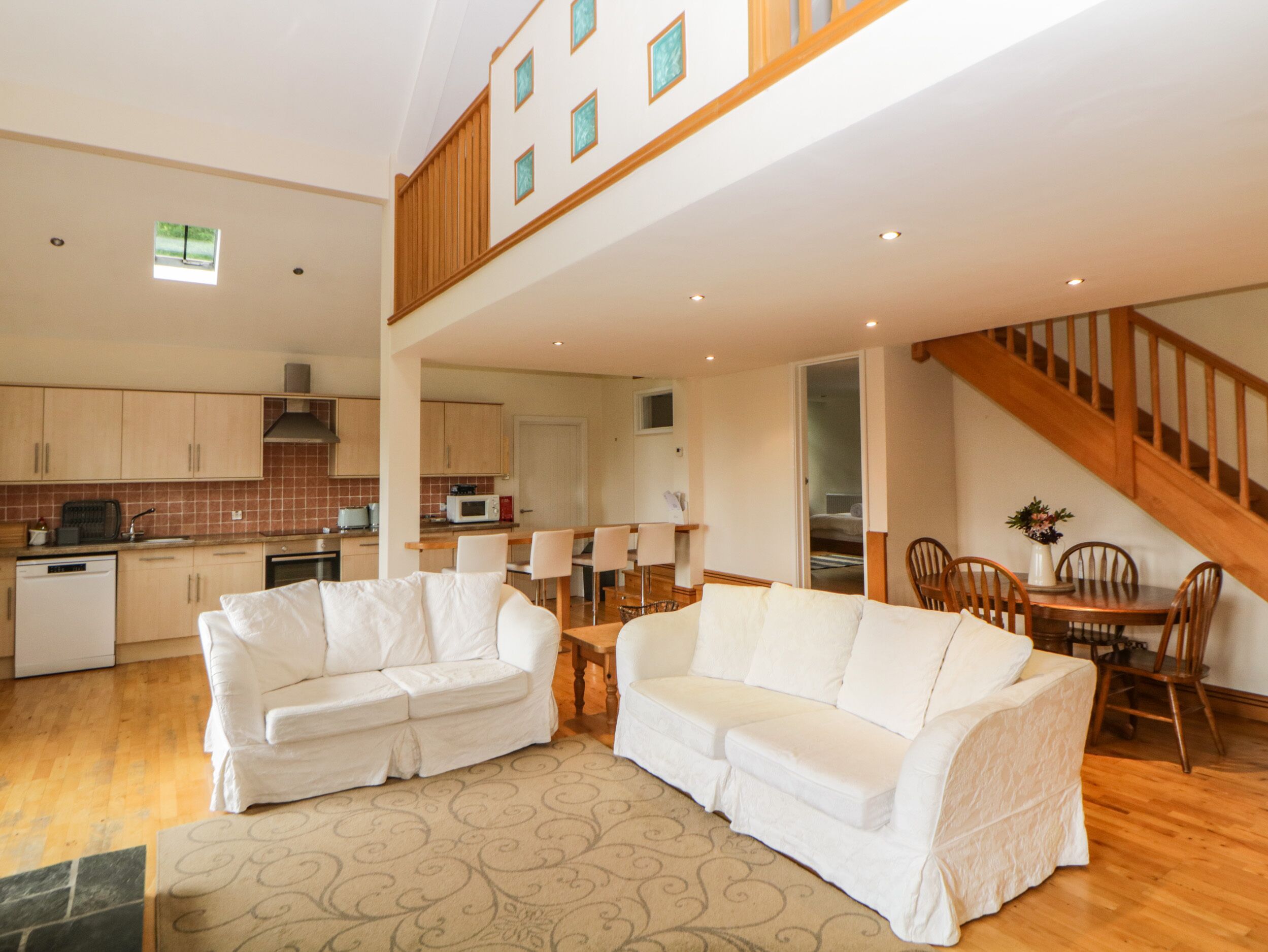 A spacious living area with a high ceiling, a kitchen in the background, and a staircase leading to an upper level.