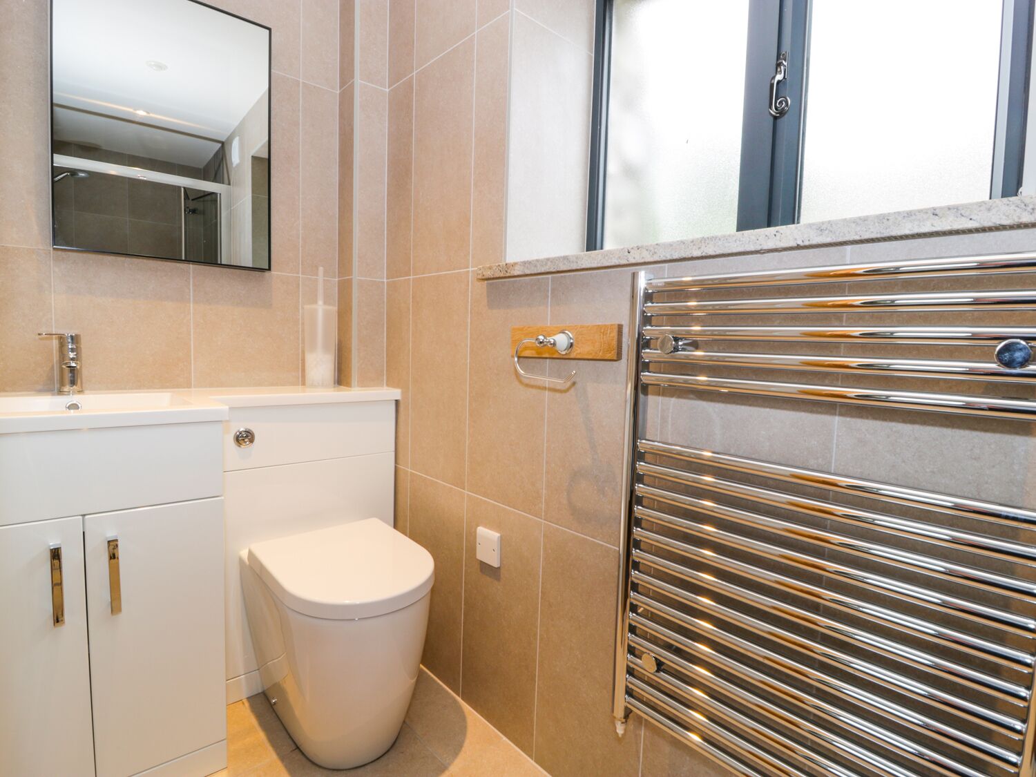 A modern bathroom with a toilet, sink, and a chrome towel rail.