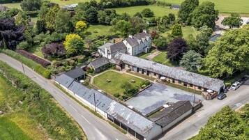 An aerial view of a large, historic building with multiple wings, surrounded by lush greenery and a well-maintained lawn.