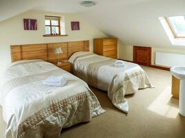 Un dormitorio con dos camas, cabeceros de madera, una mesita de noche, un aparador, un ventanal y un tragaluz.