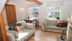 A cozy living room with two sofas, a wooden table, and a bench. There are windows with curtains and a view of the outside. - Hillside View (Hawes)