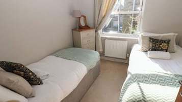 A bedroom with two beds, a bedside table with a lamp, a radiator, and a window with curtains.