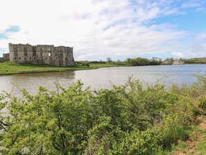 A historic stone castle by a river with lush greenery in the foreground. - Hill Top Farm Cottage (Narberth)