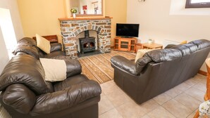 Ein Wohnzimmer mit Kamin aus Stein, Ledersofas, einem Flachbildfernseher und einem Holzschrank.
