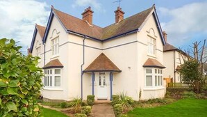 Une maison à deux étages avec une entrée centrale, un toit en briques et un jardin à l’avant, avec un chemin menant à la porte.