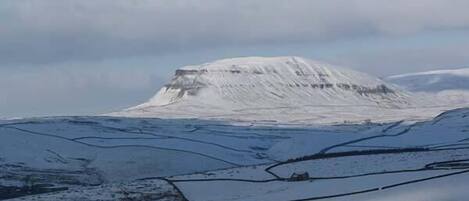 A snow-covered landscape with a prominent hill and a small structure in the distance.