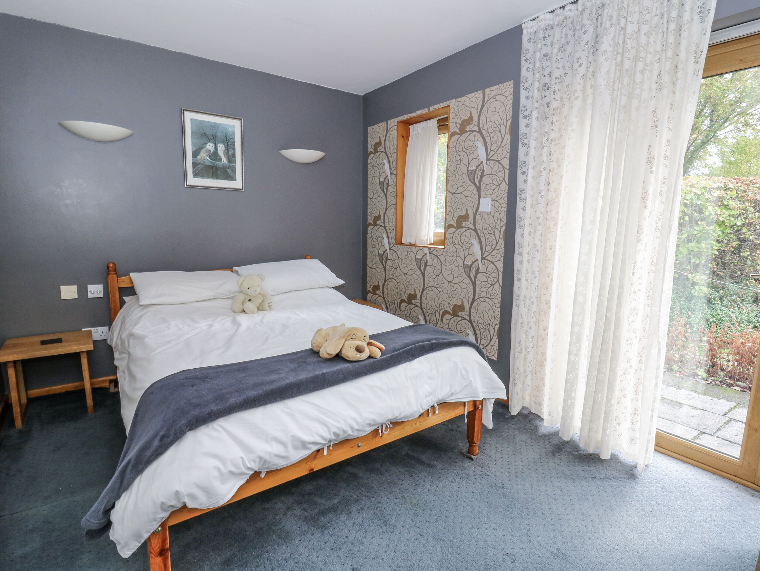 A bedroom with a bed, a nightstand, a teddy bear, a stuffed animal, and a window with curtains.