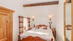 A bedroom with a wooden bed, a wardrobe, a mirror, and a nightstand with a lamp. - Bod Rhiw (Pwllheli)