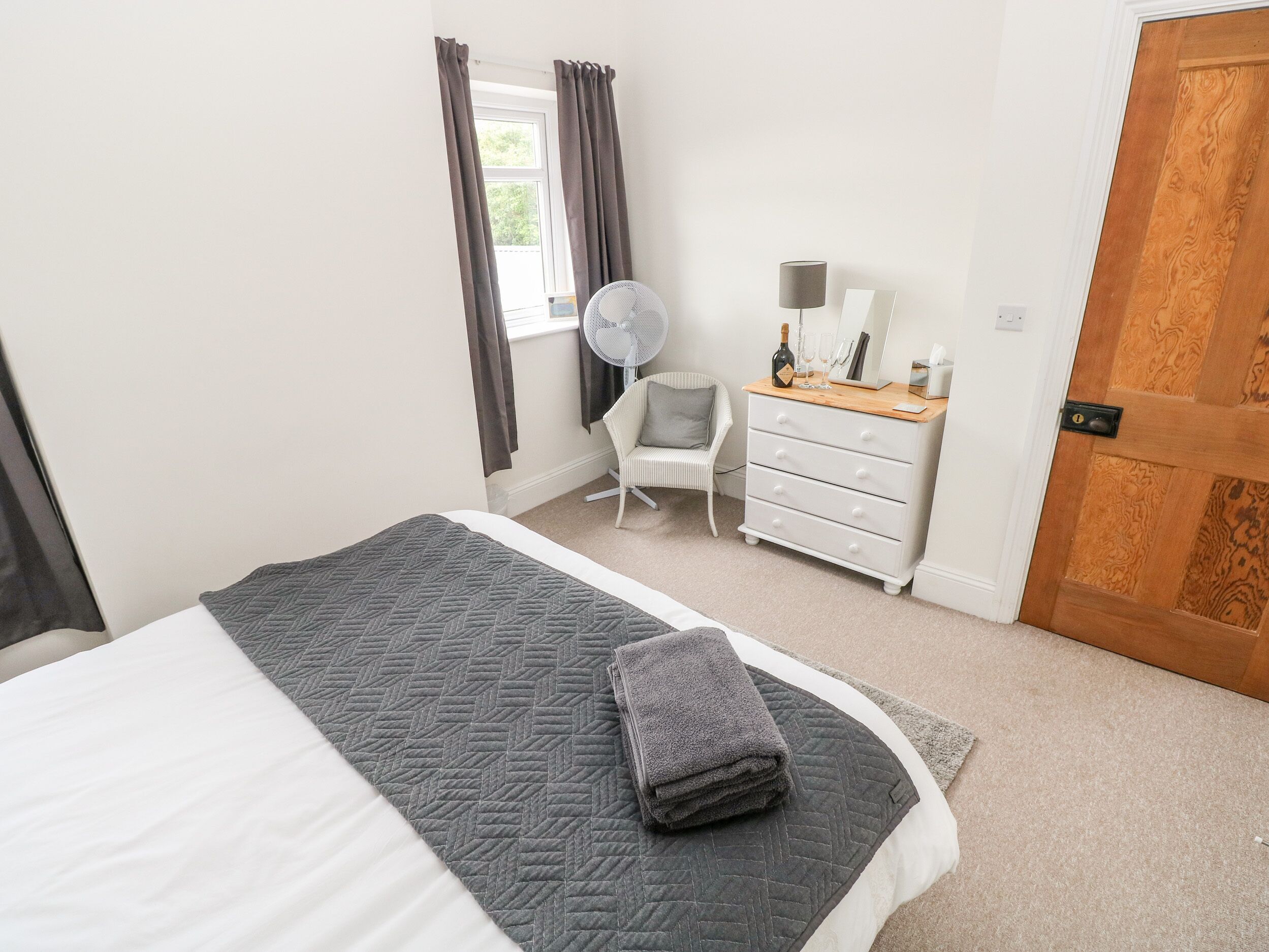 A bedroom with a bed, a dresser, a chair, a fan, and a door.