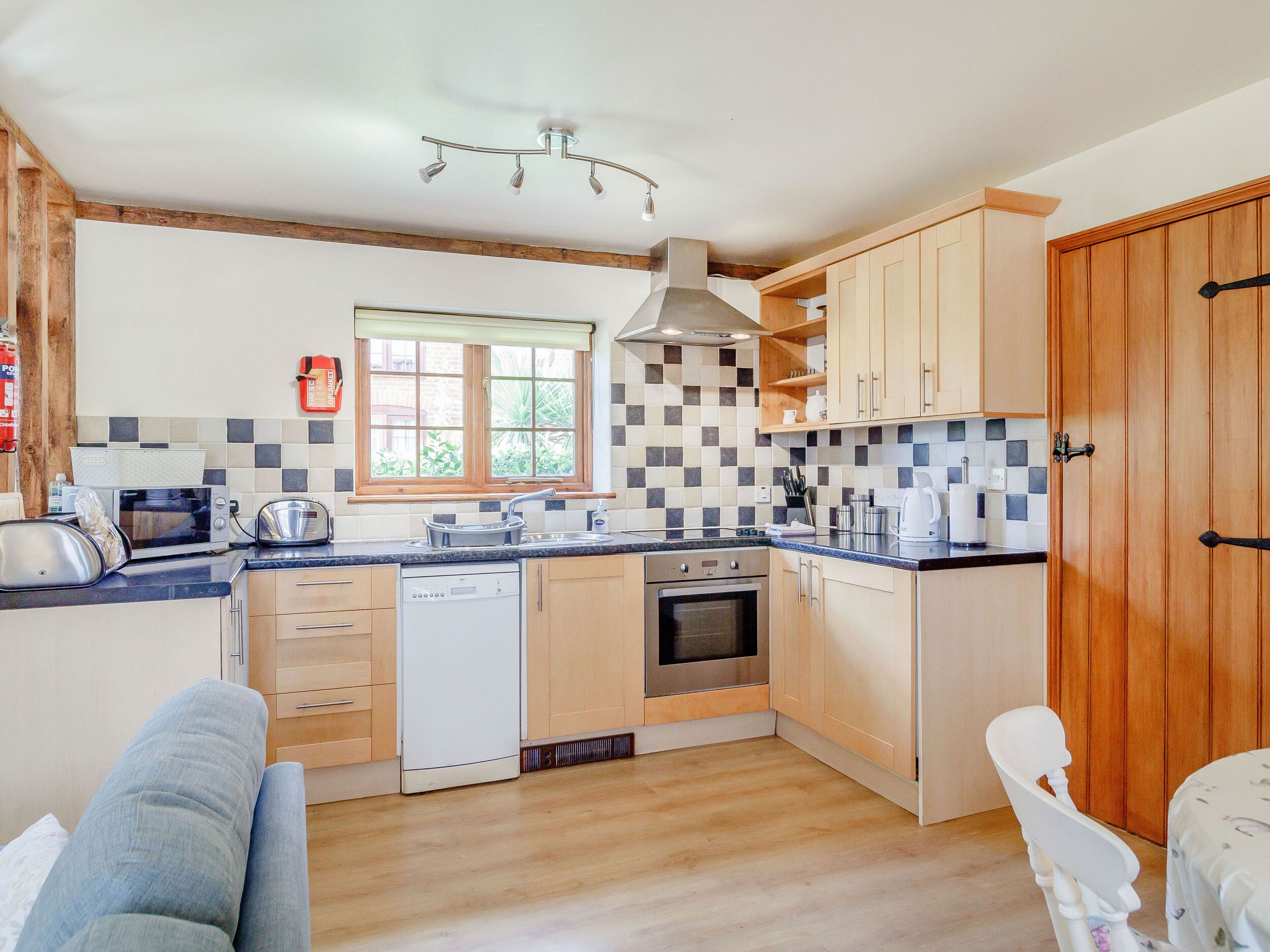 A compact kitchen with wooden cabinets, a dishwasher, a stove, and a window with a view of greenery.