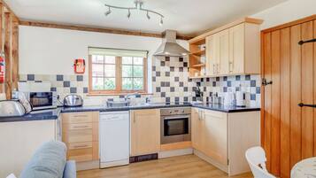 A compact kitchen with wooden cabinets, a dishwasher, a stove, and a window with a view of greenery.