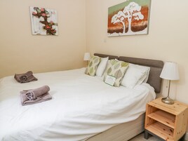 Una cama bien hecha con sábanas blancas, una mesita de noche de madera con una lámpara y dos cuadros colgados en la pared.