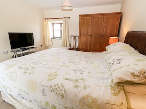 A bedroom with a large bed, a wooden wardrobe, a television on a stand, and a window with curtains.