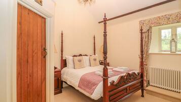 A four-poster bed with a wooden frame and a canopy, a chandelier, a window with floral curtains, and a radiator.