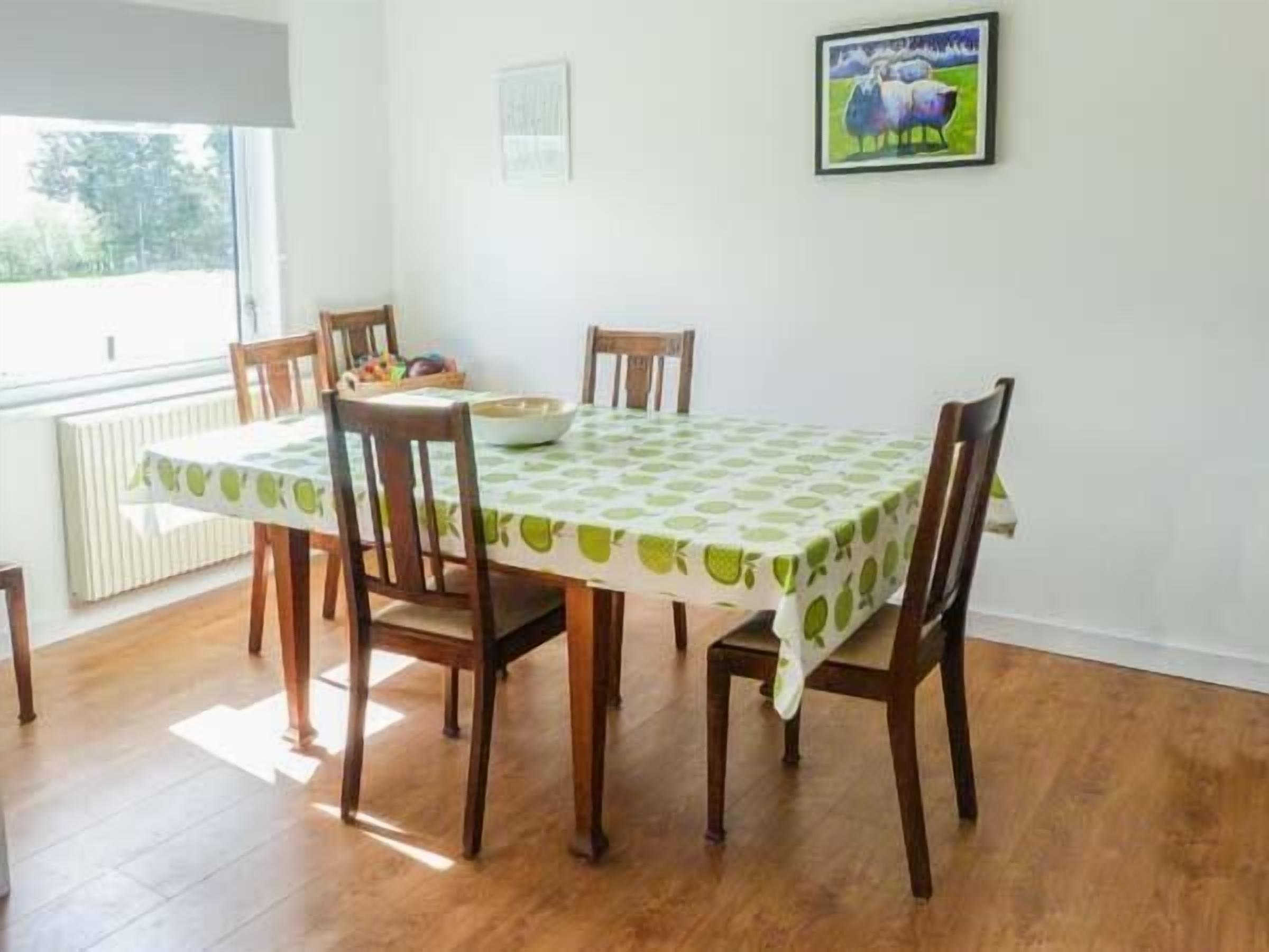 A dining area with a table covered by a green and white tablecloth, surrounded by wooden chairs.
