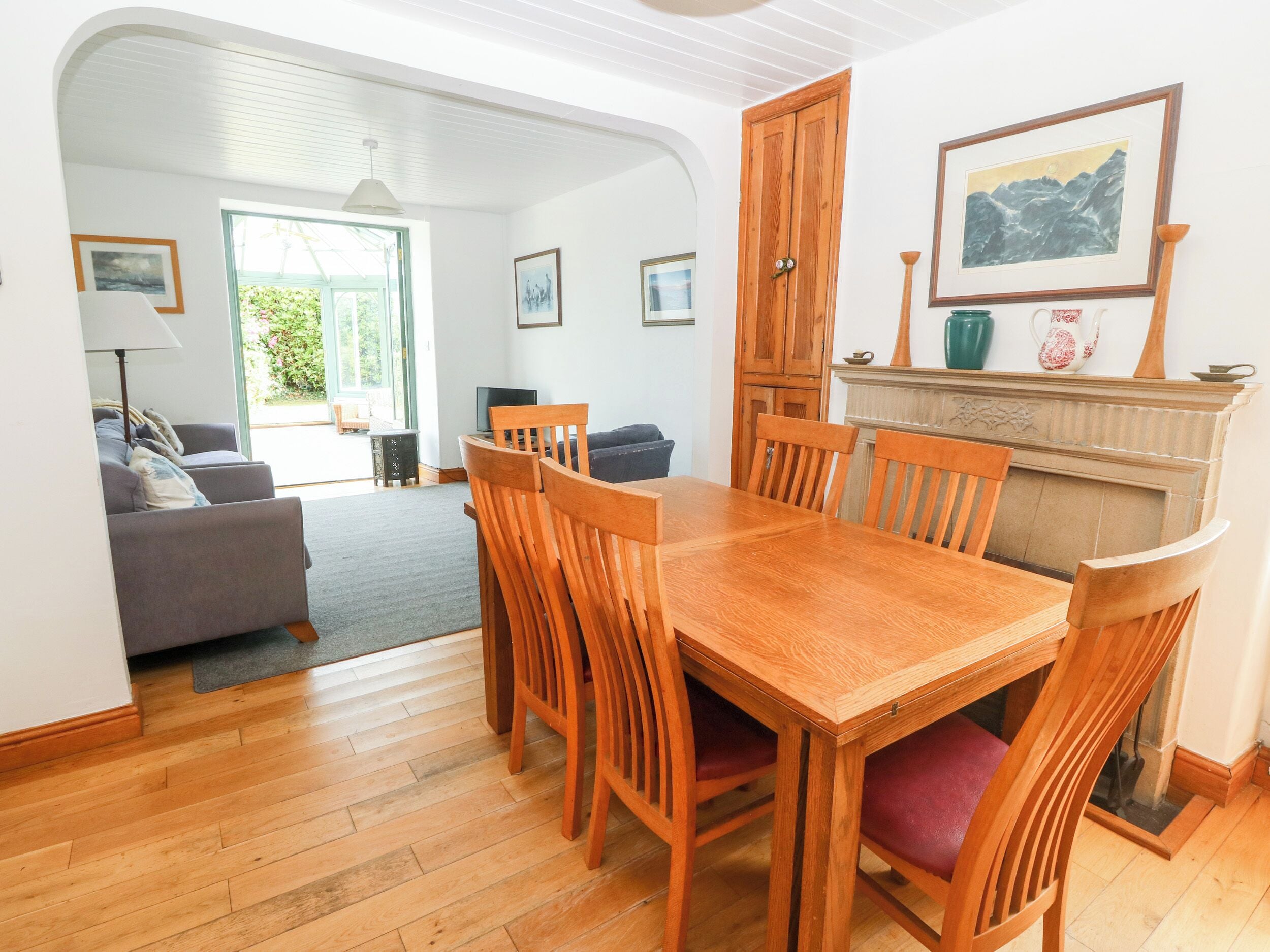 Een eetgedeelte met een houten tafel en stoelen, een bank en een open haard met een schilderij erboven.