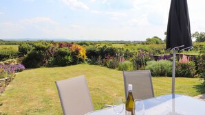 Ein Tisch mit zwei Stühlen und einer Weinflasche, draußen mit Blick auf einen Garten und ferne Hügel.