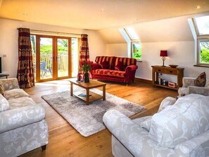 A spacious living room with a red sofa, a wooden coffee table, and a white patterned sofa. There is a large sliding glass door leading to a garden. - Brynhir Farm (Llandrindod Wells)
