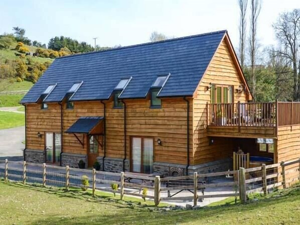 A wooden cabin with a sloped roof, a balcony, and a fenced yard. - Brynhir Farm (Llandrindod Wells)