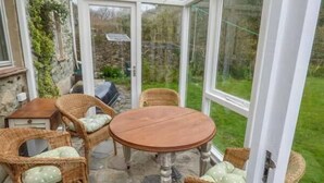 A conservatory with a stone floor, wicker furniture, and a view of the garden. - Court House (Haverfordwest)