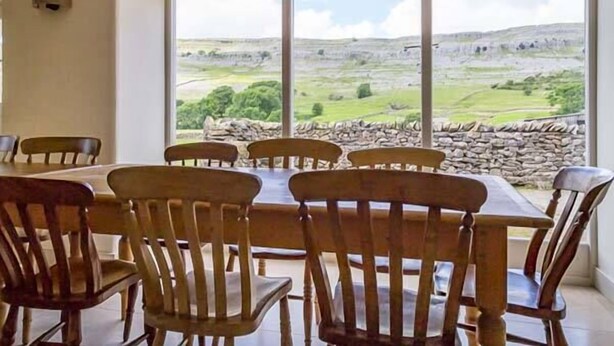 A dining area with a table and chairs, large windows with a view of a rural landscape. - Dale House Farm Cottage (Carnforth)