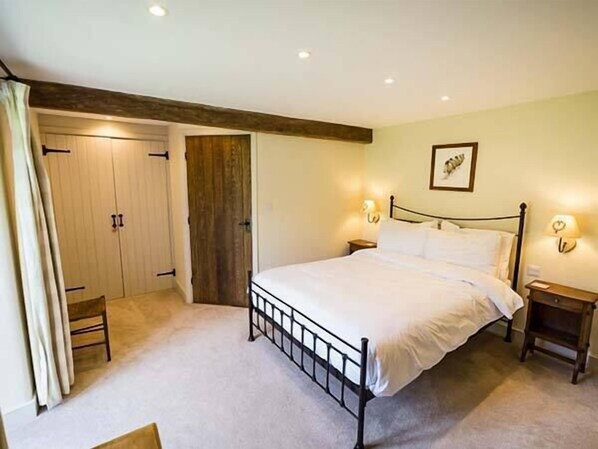 A bedroom with a bed, bedside tables, a wardrobe, and a door. - Dale House Farm Cottage (Carnforth)