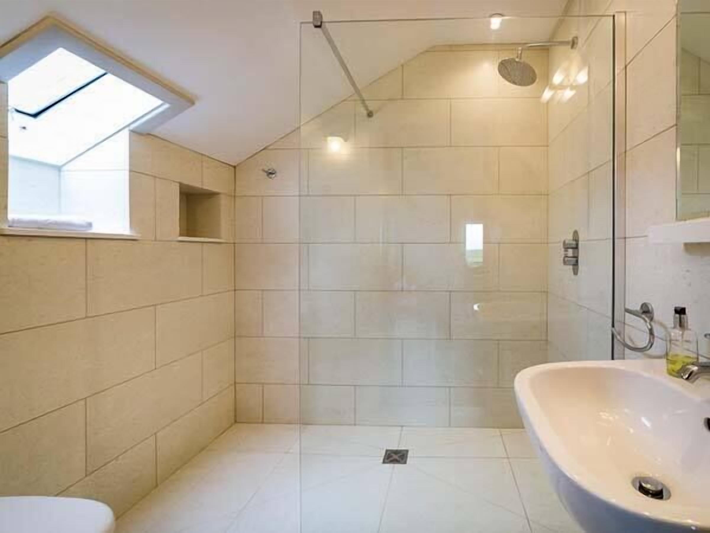 A modern bathroom with a glass-enclosed shower, a large sink, and a skylight.